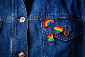 LGBTQIA pins on a jean jacket representing individuals who identify as LGBTQ and autistic. Learn more from an autism therapist in Palo Alto, CA who offers online autism therapy in California at Open Doors Therapy