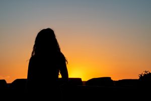 woman with autism sits in the shadows and watches the sunset marking a new beginning and the end of comparisons with neurotypical people. Learn more from an autism therapist who offers online autism therapy in California at Open Doors Therapy